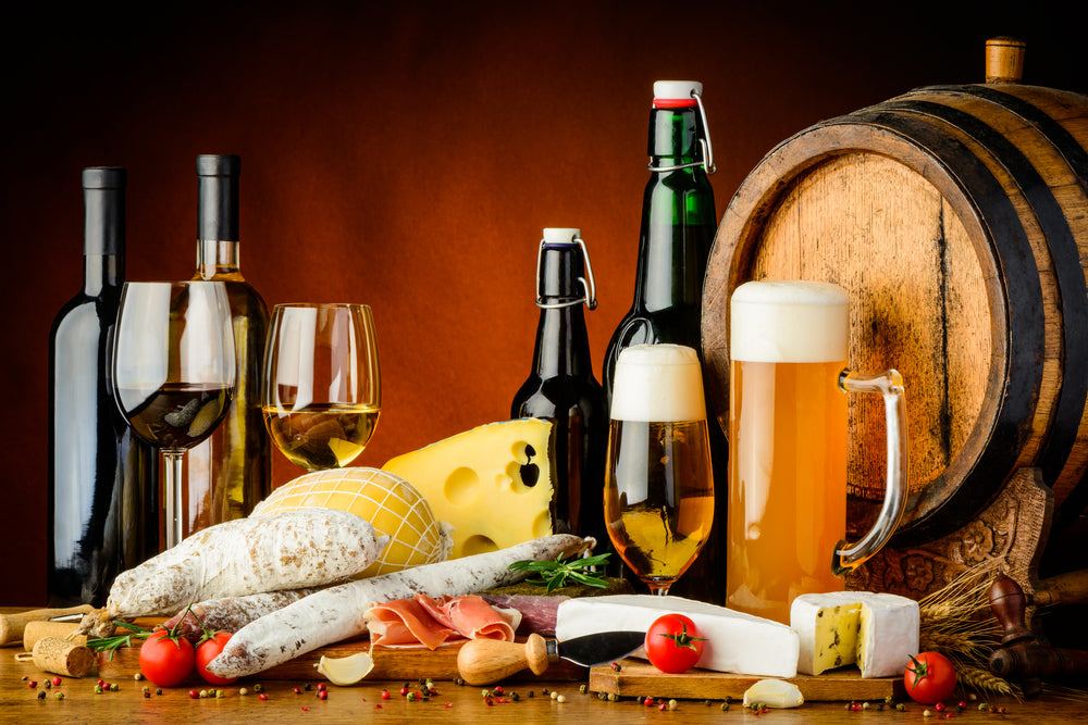 A selection of wine, beer, cheese, and sausages displayed on a rustic wooden table.